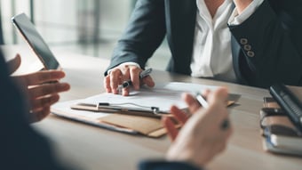 A photo of a business meeting between two people with only their hands visible and a clipboard between them.
